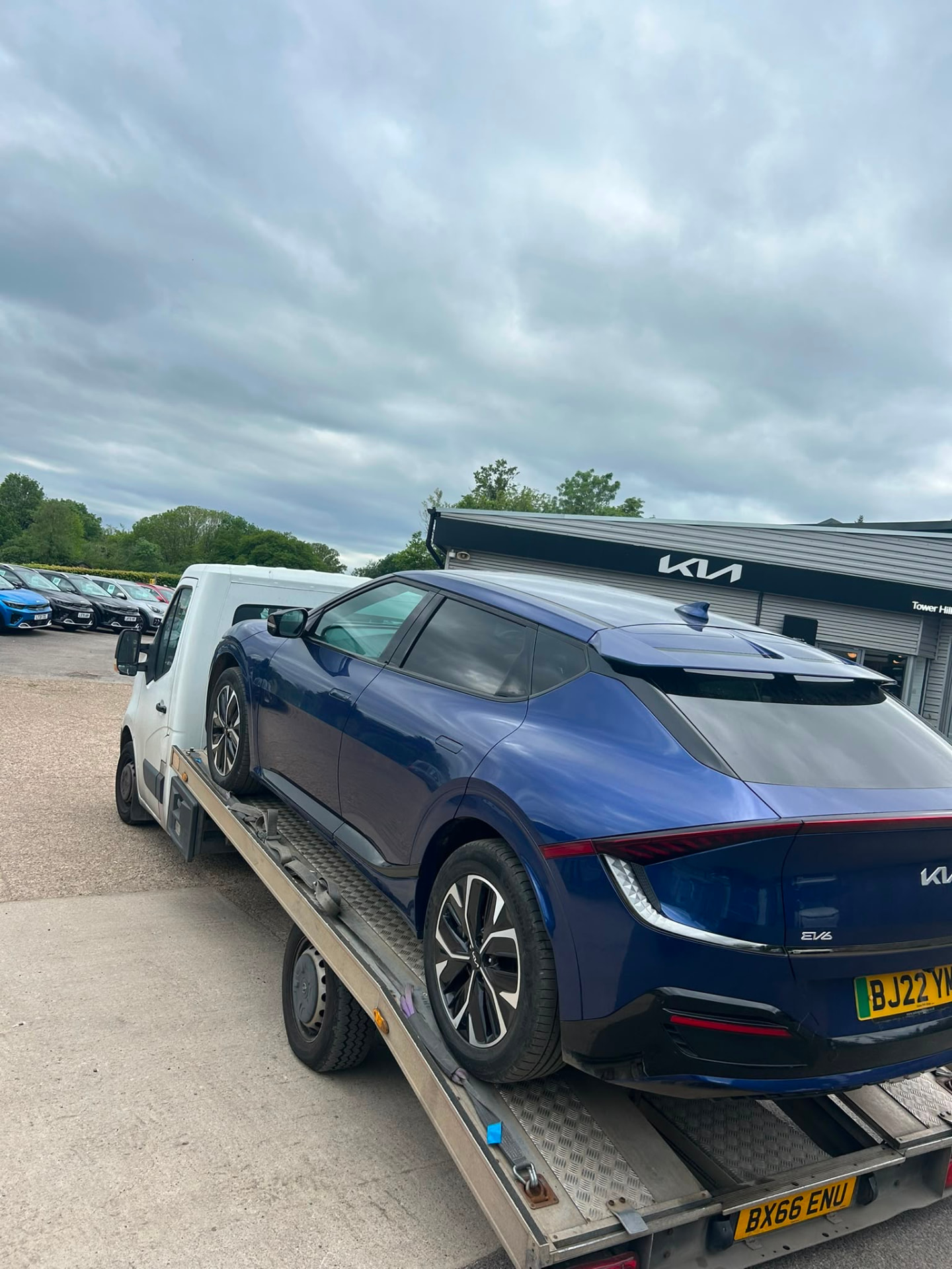 Blue Kia EV6 loaded onto a recovery truck at a dealership